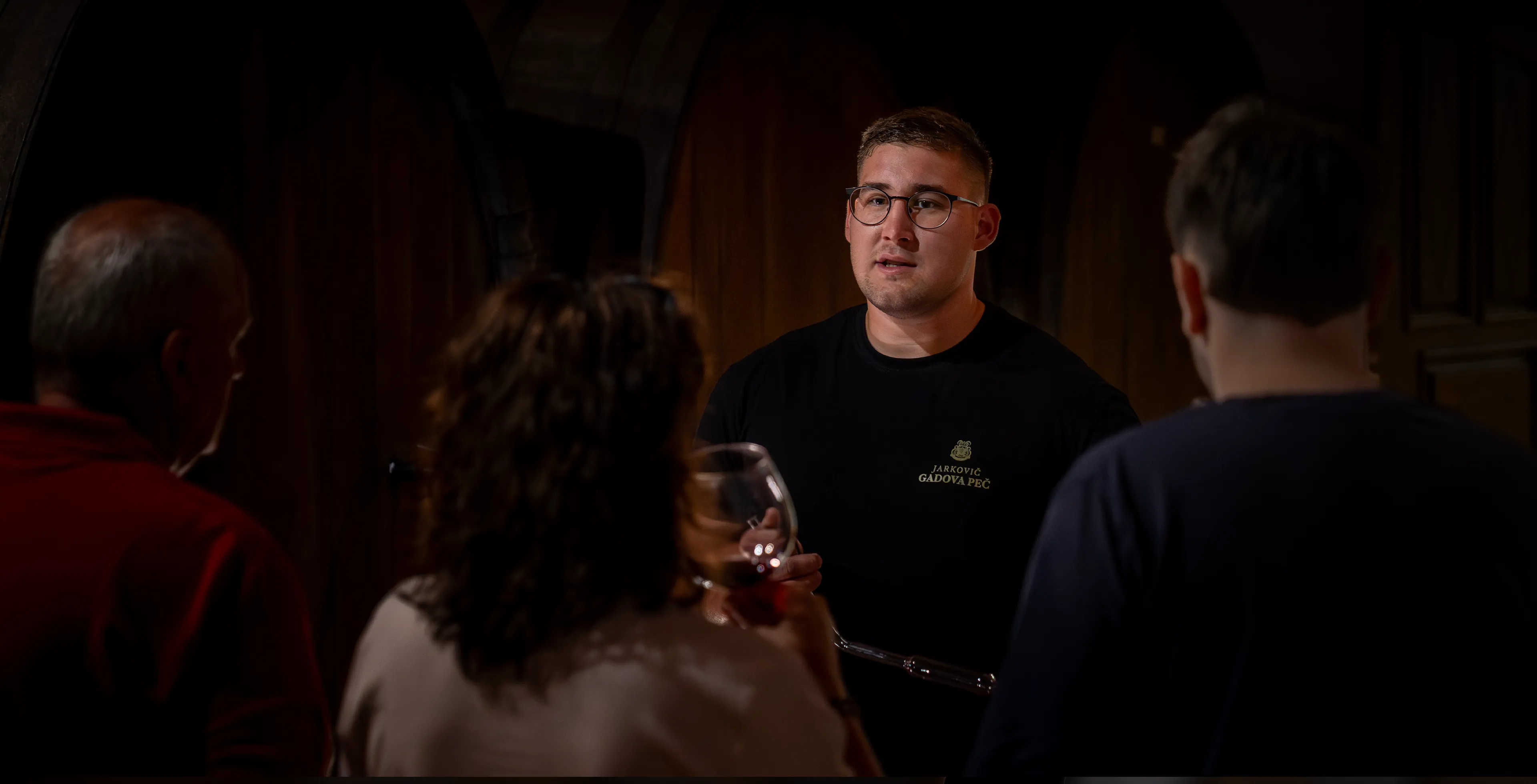 Guests and the winemaker raising glasses and tasting wine among wooden barrels in the Jarkovič cellar