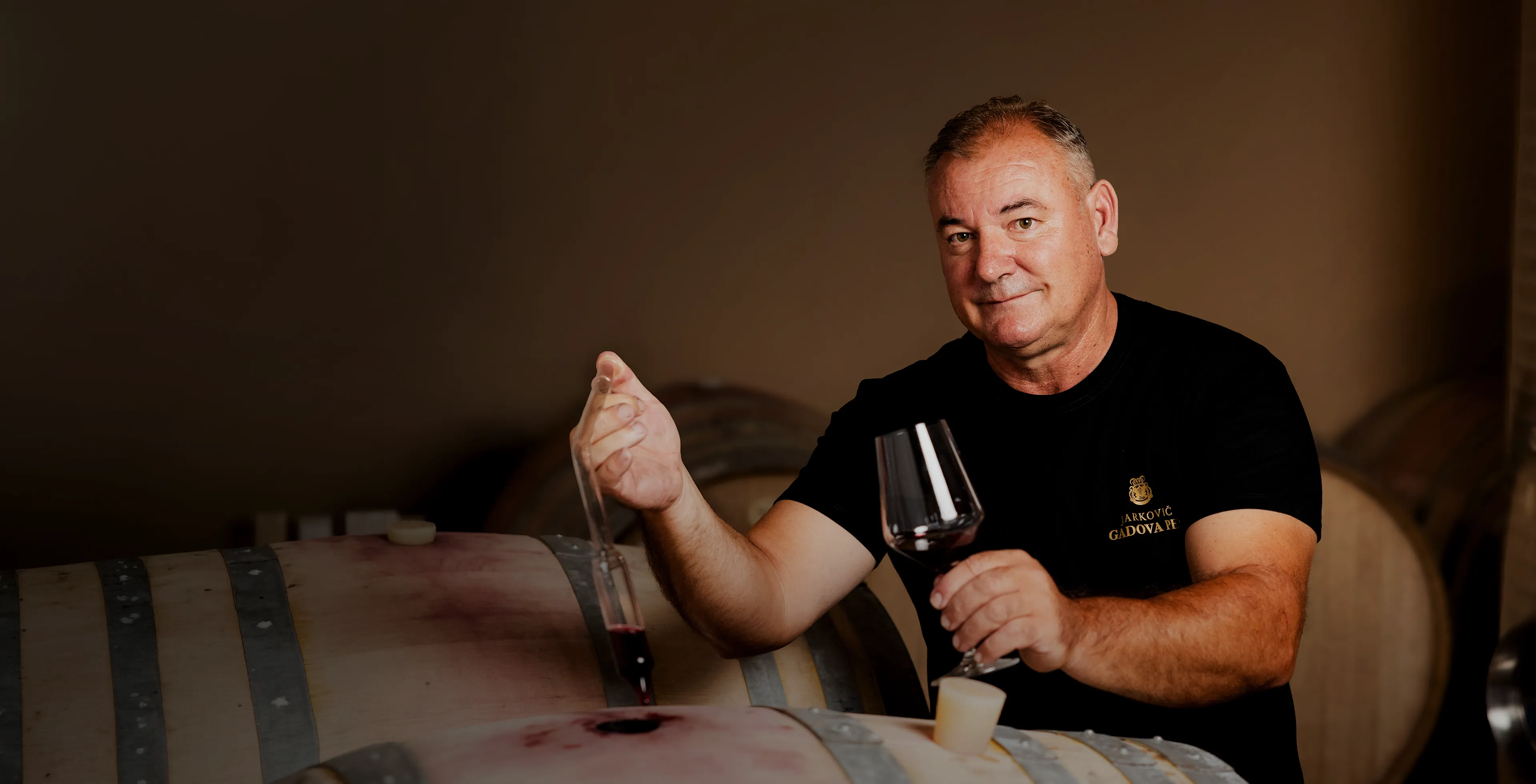 Winemaker Jarkovič checking the colour of red wine in his glass in a dim cellar between stainless steel tanks